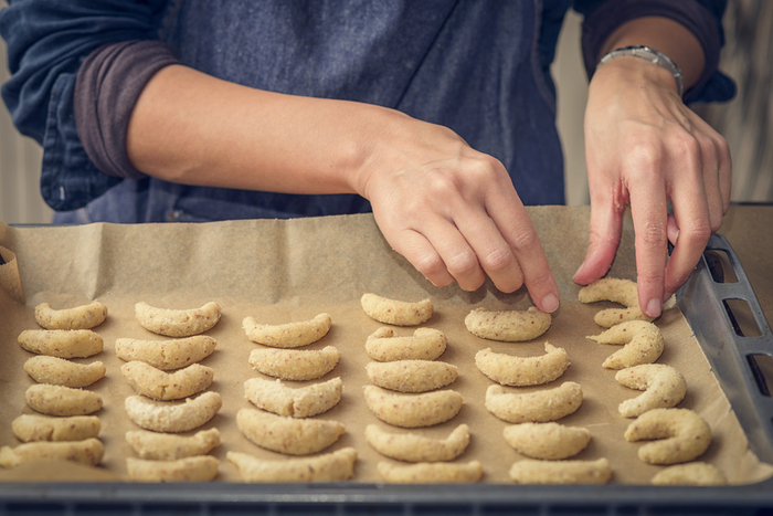 Mensch bereitet traditionelle Halbmondkekse für Weihnachten und die festliche Jahreszeit zu und bereitet den Teig auf einem Backblech zum Backen vor. Nahaufnahme der Hände