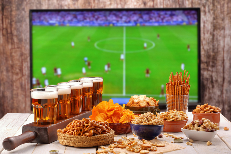 Ein Tablett mit frisch gezapftem Bier steht vor einem Fernseher, auf dem ein Spiel der Europameisterschaft läuft.