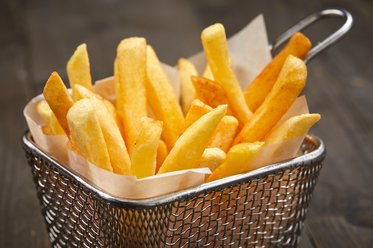 In einem Drahtkorb steckt eine Portion frittierte Pommes.