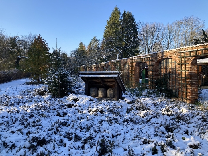 Bienenkörbe im Schnee, im Hintergrund Gartenmauer