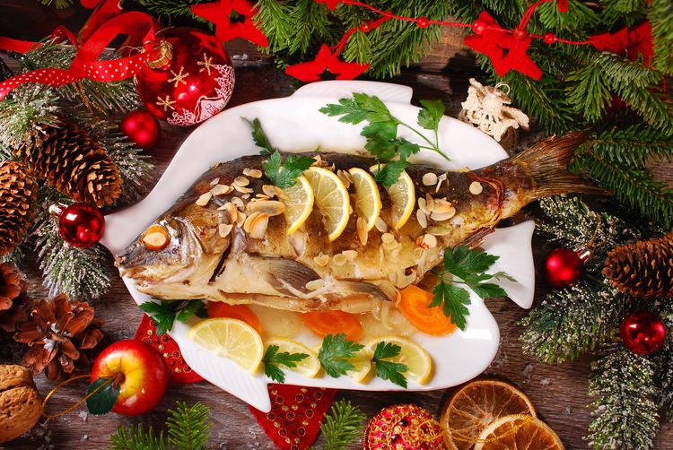 Fisch weihnachtlich dekoriert auf einem Fischteller mit Zitrone und Mandeln